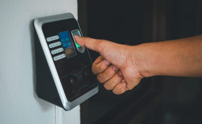 A person is using a fingerprint reader to access a building A person is using a fingerprint reader to access a building. The device is black and silver. The person is touching the screen with their finger